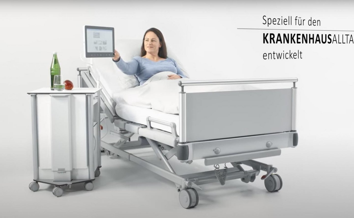 BEWATEC.Nachttischschwenkarm GFK – Patientin im Krankenhausbett dreht Bedside Terminal an Nachttischhalterung