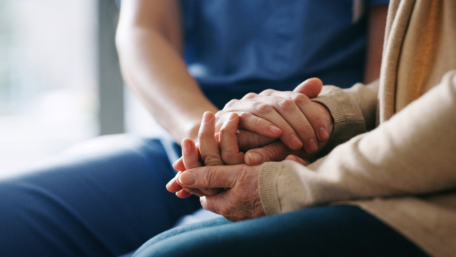 Pflegekraft hält Hand von älterer Patientin.