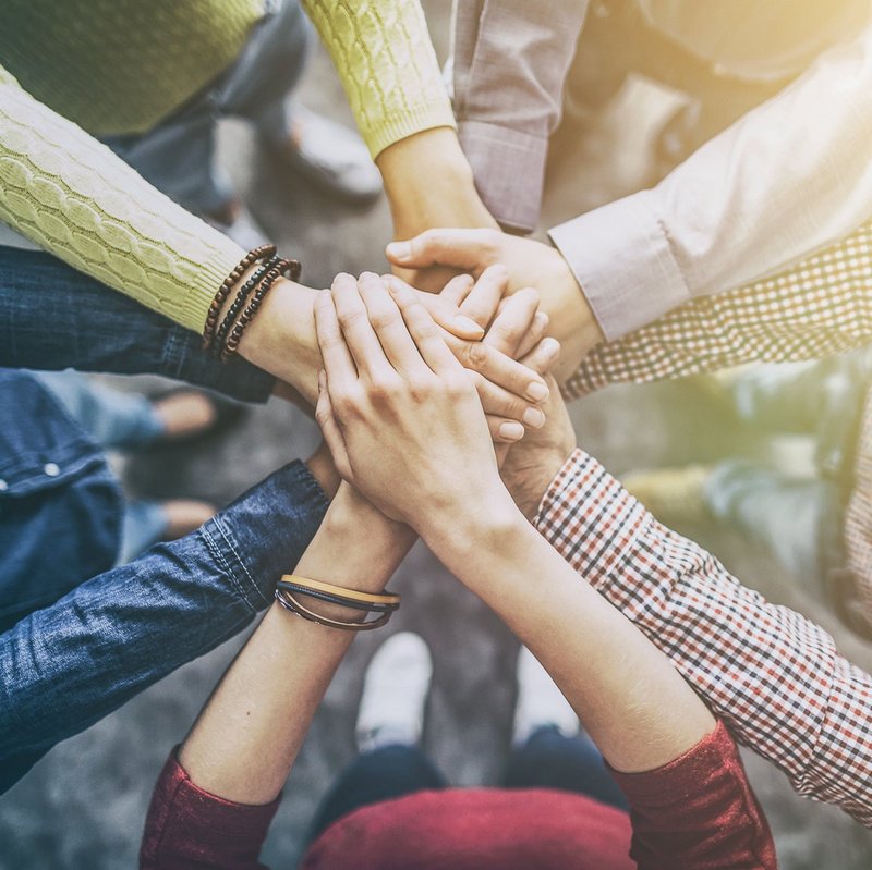 Teamwork: Mitarbeiter stehen im Kreis und legen Hände aufeinander