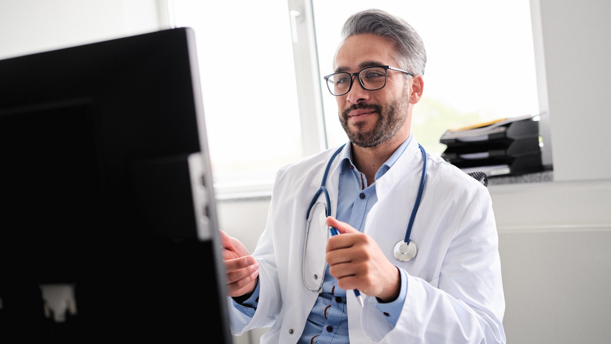 Arzt sitzt am Rechner und hält Video-Visite mit Patienten