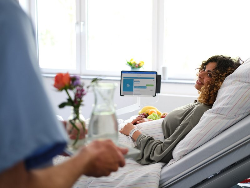 Patientenkommunikation: Pfleger bringt junger Patientin Wasser ans Bett, das sie über den digitalen Service Call bestellt hat.