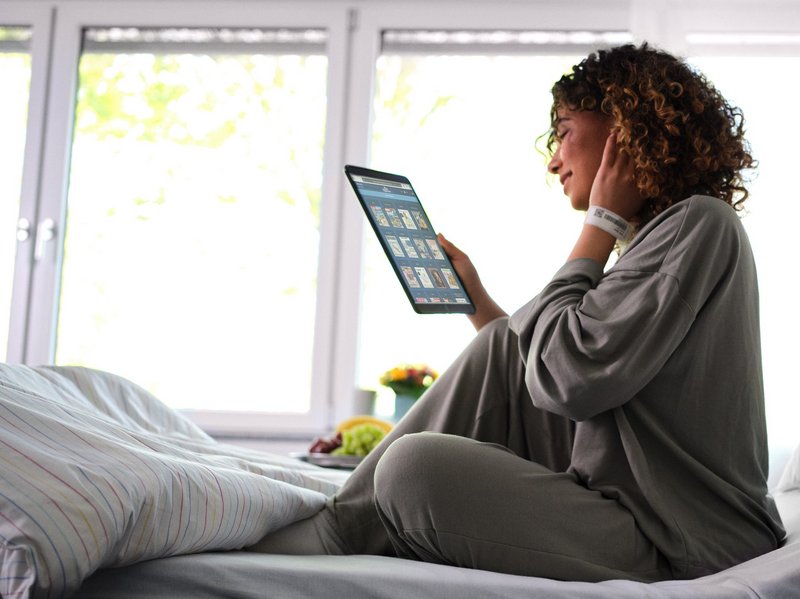 Patientenentertainment: Junge Patientin sitzt im Krankenhausbett und liest eMagazine von sharemagazines auf Tablet