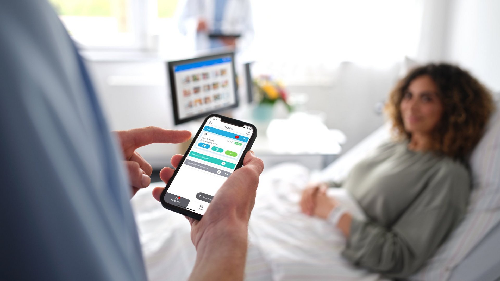 Digitale Patientenkommunikation: Pfleger steht am Patientenbett einer jungen Frau und bedient Smartphone mit dem Digitalen Serviceruf.