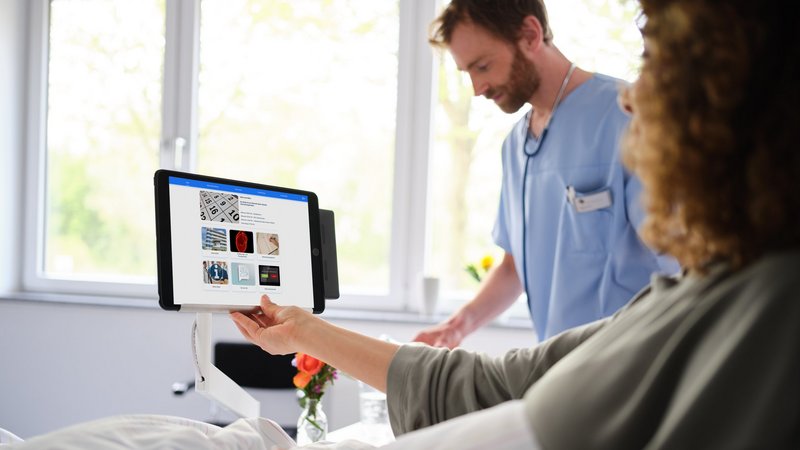 Krankenhaus digitalisieren: Patientin im Krankenhausbett bedient iPad mit eHealth Plattform BEWATEC.ConnectedCare, BEWATEC iPad-Halterung am Nachttisch