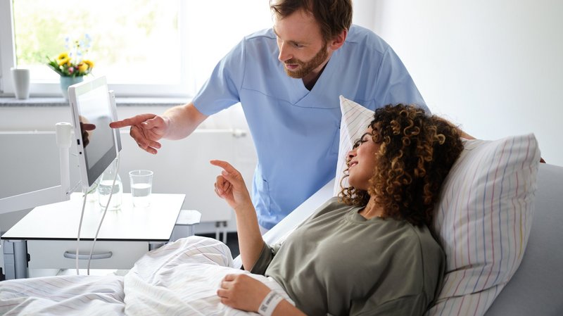 Patient Engagement: Pfleger zeigt junger Patientin etwas auf dem Bedside Terminal von BEWATEC