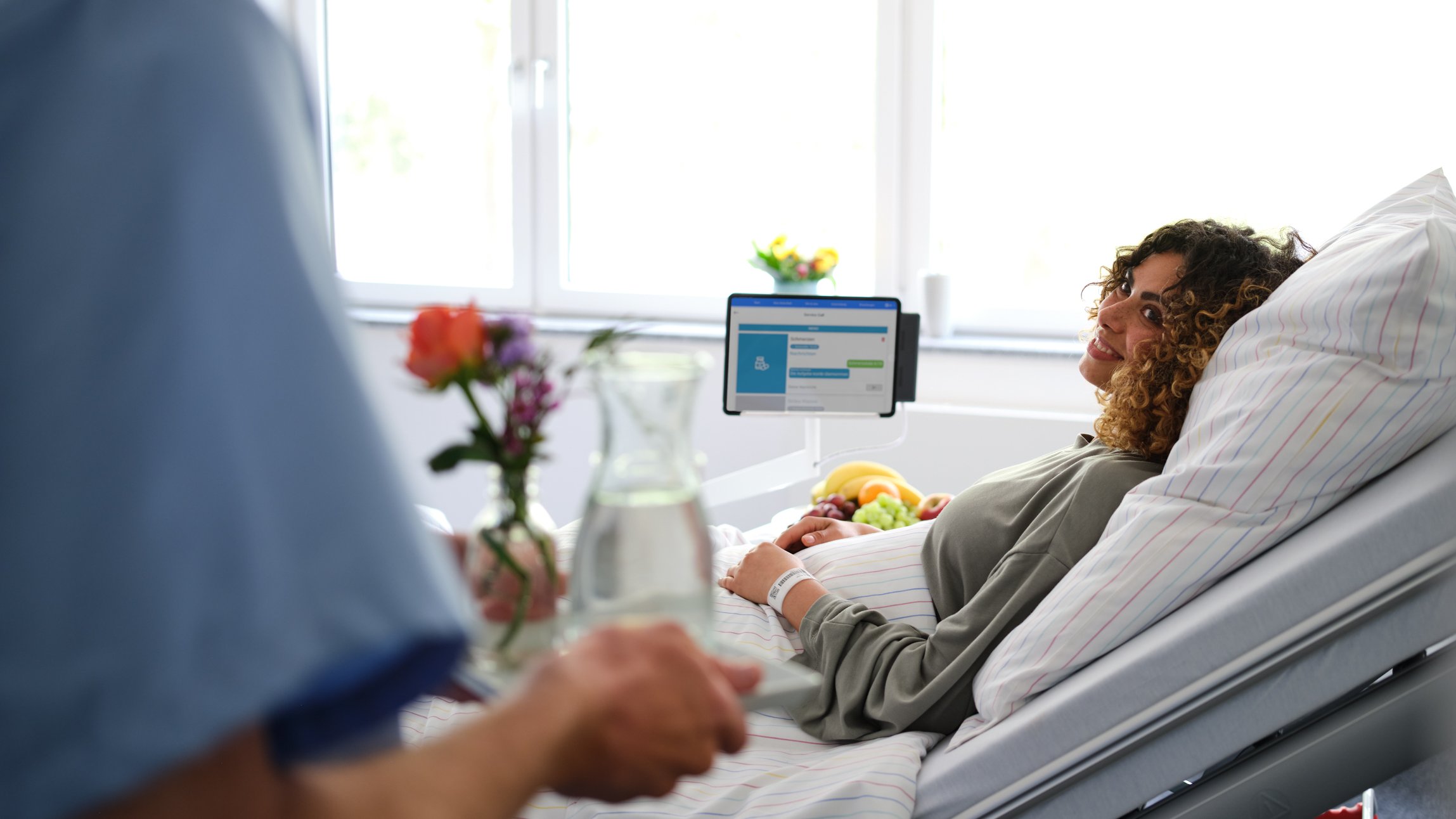 Patientenkommunikation: Pfleger bringt junger Patientin Wasser ans Bett, das sie über den digitalen Service Call bestellt hat.